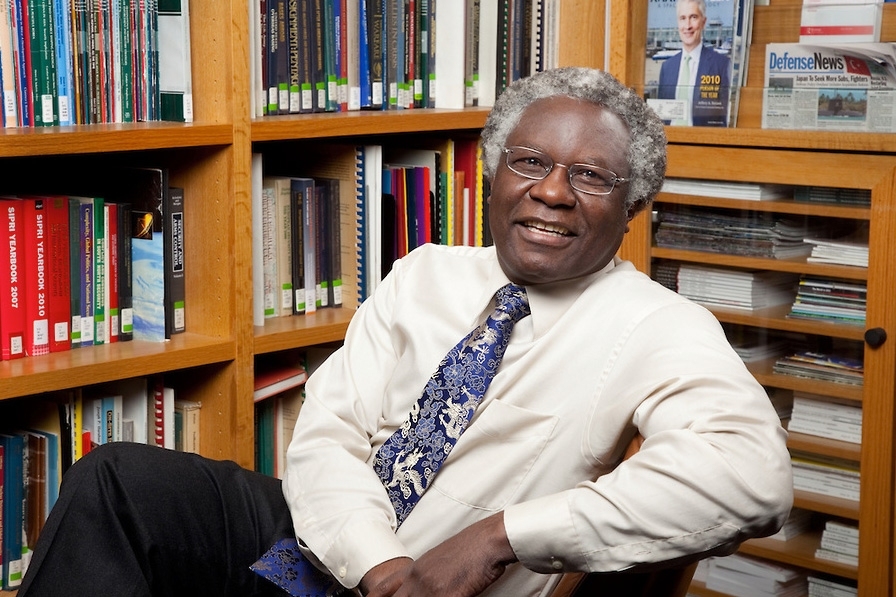 Calestous Juma leans back in a chair, with bookshelves in the background.