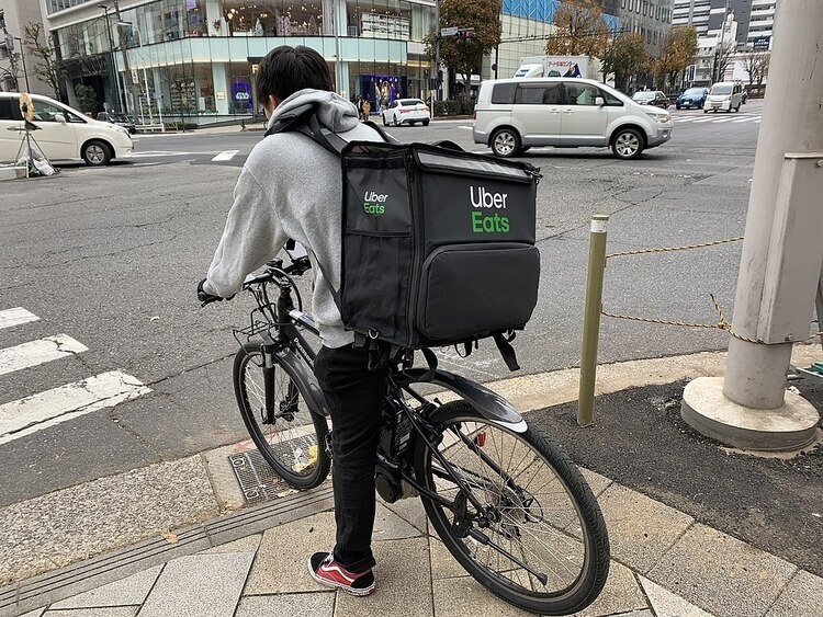 A cyclist with an UberEats backpack stands at a crosswalk.